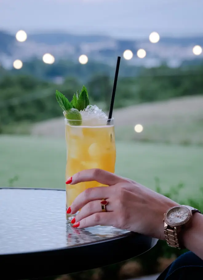 realistic photo of a woman's hand holding a refreshing drink in her hand with the nature greenery as a blurred background